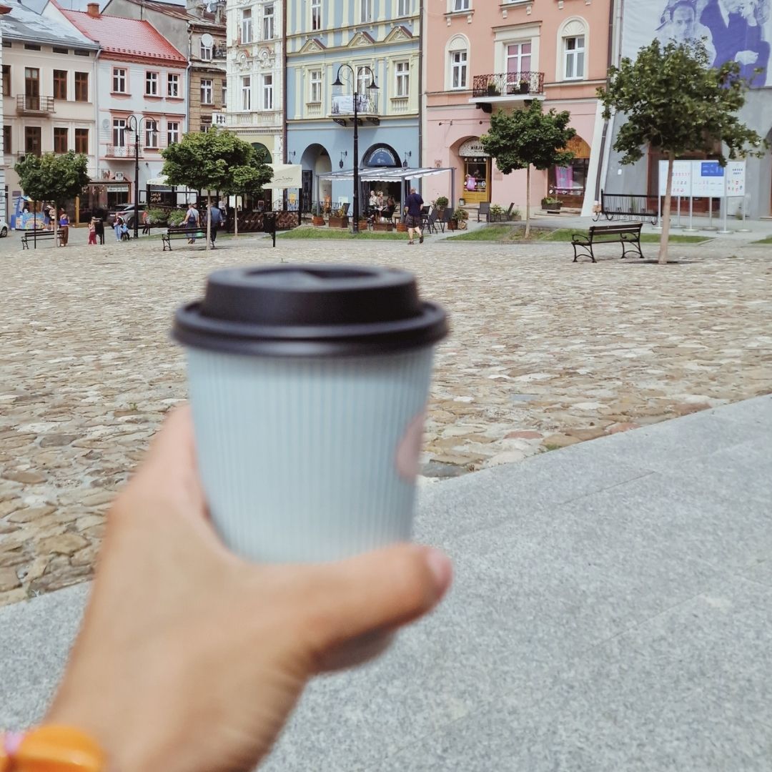 Dłoń trzymająca kubek kawy na tle kolorowego rynku.